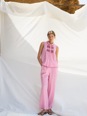 legante y fresco conjunto de dos piezas confeccionado en tejido ligero de color blanco, realzado con delicados bordados en azul que aportan un aire artesanal y sofisticado. El top presenta un diseño femenino y favorecedor que combina a la perfección con el pantalón de corte fluido, creando una silueta cómoda y estilizada. El contraste entre el blanco luminoso y los detalles bordados en azul evoca un estilo mediterráneo, ideal para eventos de día, vacaciones, comidas especiales o celebraciones de primavera y verano. Una propuesta versátil y atemporal que destaca por su elegancia natural y sus cuidados acabados.