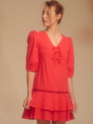 estido corto rojo de estampado a cuadros, con un diseño femenino y llamativo. Presenta mangas abullonadas que aportan volumen y un toque romántico al conjunto. Su corte corto realza la silueta y lo convierte en una prenda fresca y versátil, ideal para ocasiones informales o salidas de día.